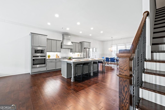 kitchen with a center island with sink, light countertops, custom range hood, gray cabinetry, and appliances with stainless steel finishes