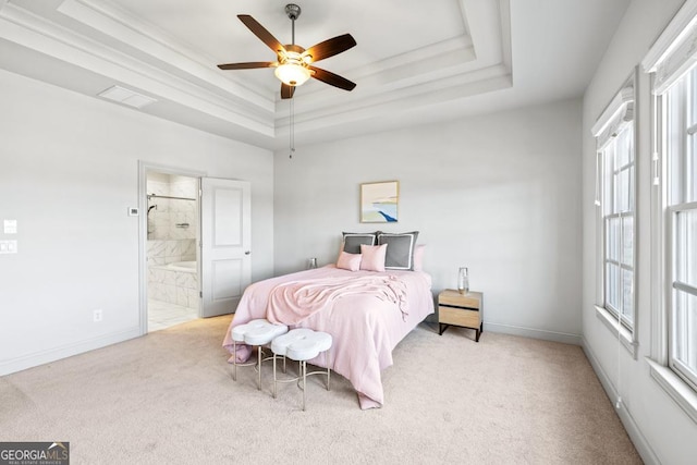 carpeted bedroom featuring a tray ceiling, ensuite bathroom, a ceiling fan, ornamental molding, and baseboards