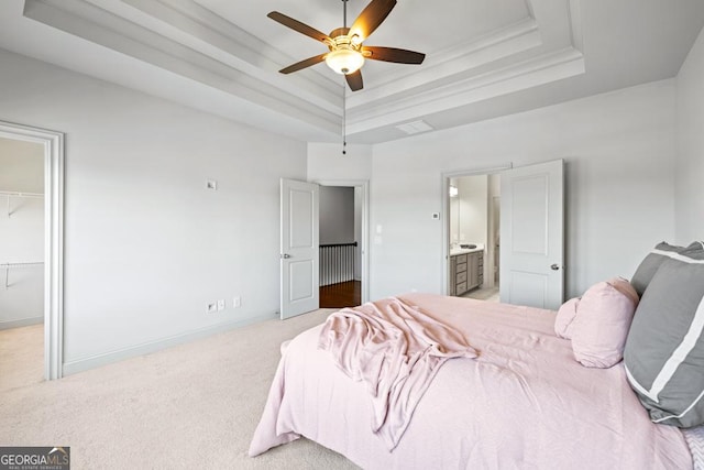 bedroom featuring a tray ceiling, carpet, a spacious closet, ensuite bath, and baseboards