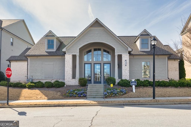 view of front of home featuring brick siding, a shingled roof, and french doors