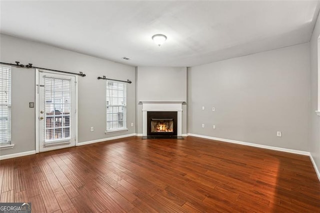 unfurnished living room with a fireplace with flush hearth, baseboards, and wood finished floors