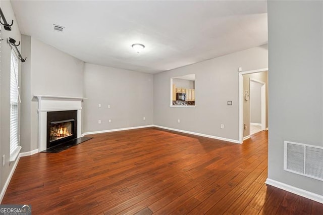 unfurnished living room with a wealth of natural light, visible vents, a glass covered fireplace, wood finished floors, and baseboards