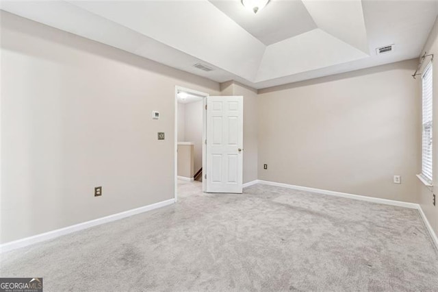 empty room with a raised ceiling, visible vents, light carpet, and baseboards