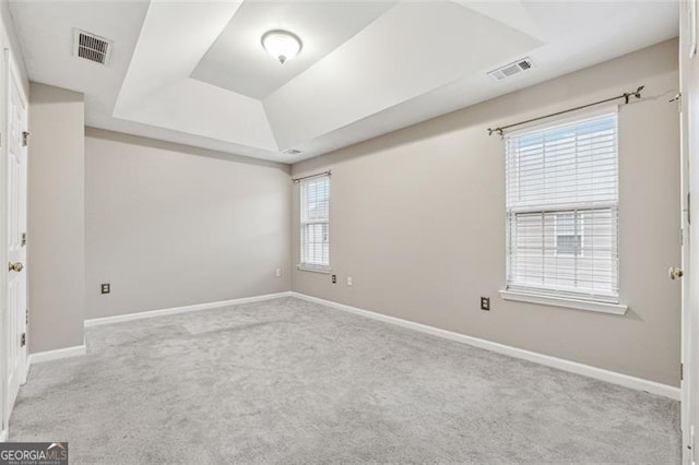 empty room with light colored carpet, a tray ceiling, visible vents, and baseboards