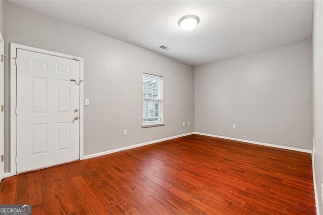 empty room featuring wood finished floors, visible vents, and baseboards