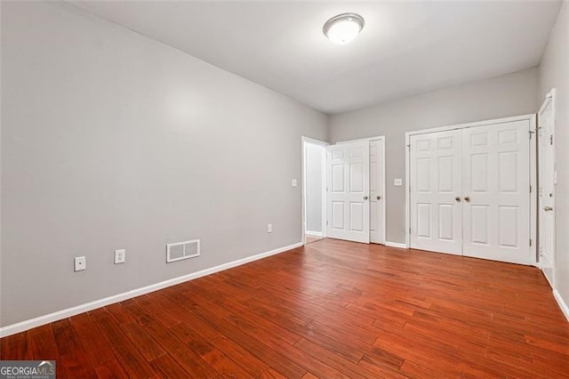 unfurnished bedroom featuring two closets, wood finished floors, visible vents, and baseboards