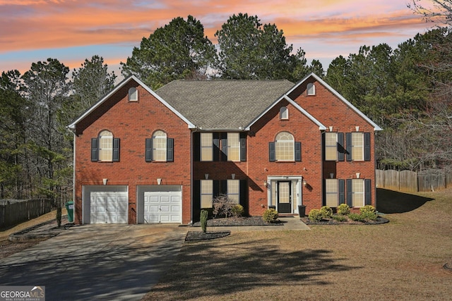 colonial inspired home with a garage, concrete driveway, a lawn, fence, and brick siding