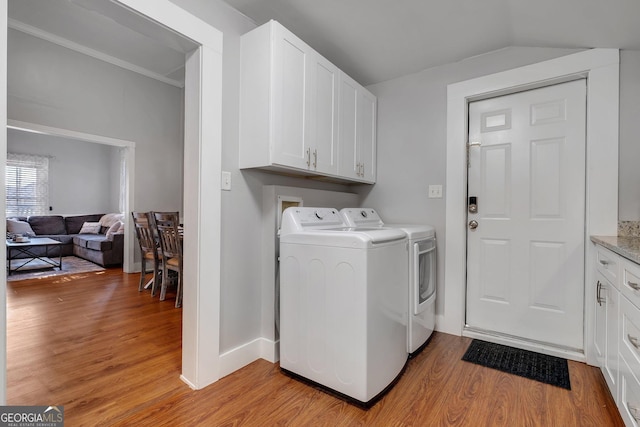 laundry area with light wood-type flooring, cabinet space, ornamental molding, and washer and dryer