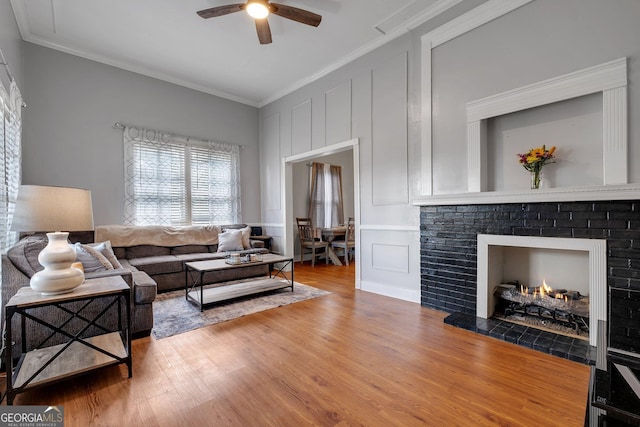 living area featuring crown molding, ceiling fan, wood finished floors, and a decorative wall