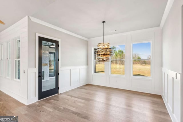 unfurnished dining area with a chandelier, a decorative wall, wood finished floors, wainscoting, and crown molding