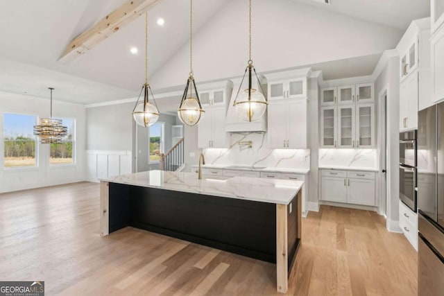 kitchen featuring hanging light fixtures, glass insert cabinets, white cabinets, an island with sink, and light stone countertops