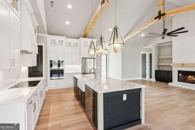 kitchen featuring glass insert cabinets, decorative light fixtures, a kitchen island with sink, stainless steel appliances, and white cabinetry