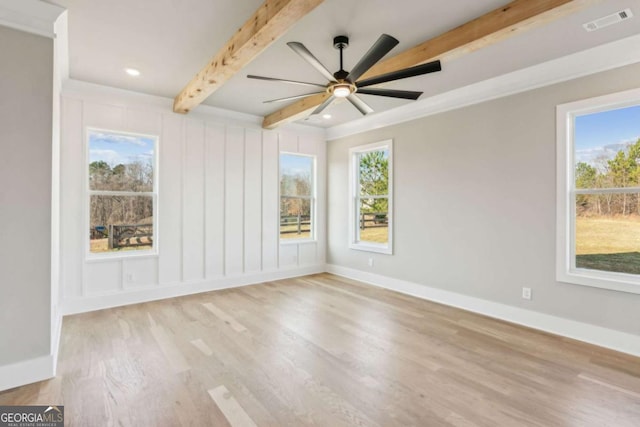 empty room with a healthy amount of sunlight, light wood finished floors, baseboards, and beamed ceiling