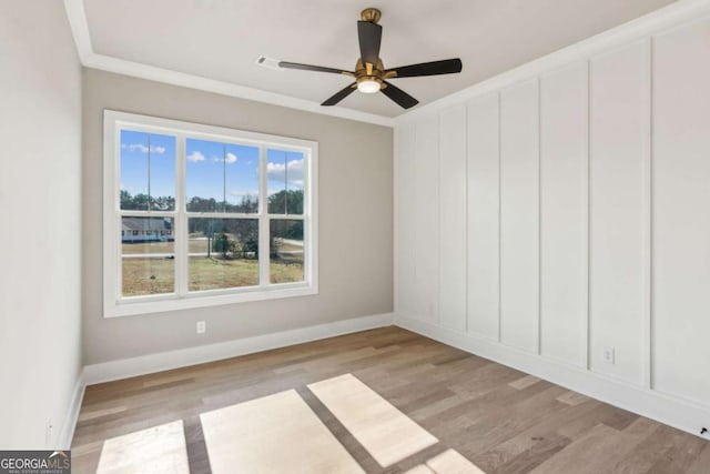 unfurnished room with crown molding, light wood finished floors, a decorative wall, ceiling fan, and baseboards