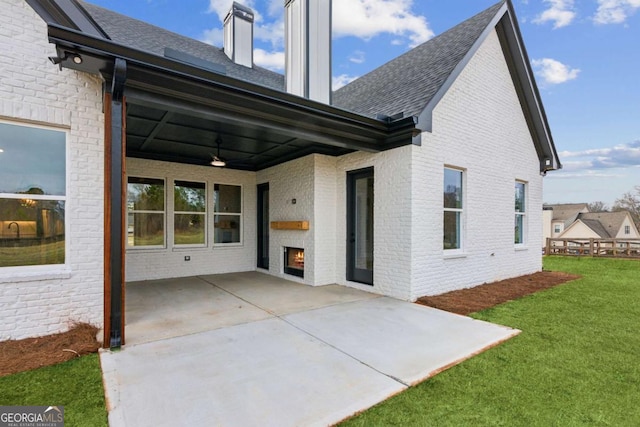 rear view of property with a patio, brick siding, a shingled roof, a ceiling fan, and a yard