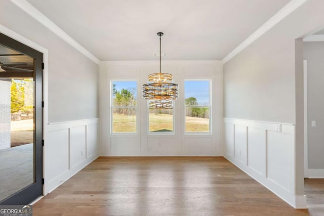 unfurnished dining area with crown molding, a decorative wall, light wood-style flooring, and an inviting chandelier