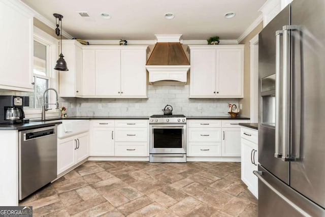 kitchen featuring dark countertops, custom range hood, decorative light fixtures, stainless steel appliances, and a sink