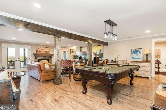 playroom featuring light wood-type flooring, french doors, crown molding, and a stone fireplace