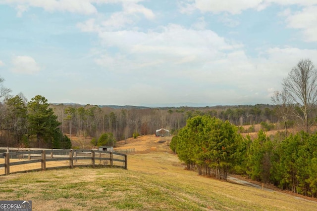 view of yard with a rural view, fence, and a view of trees