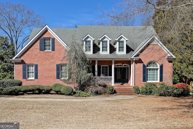 cape cod house with a porch, a front yard, and brick siding