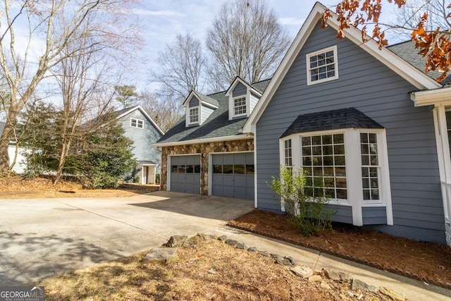 view of side of property with stone siding, driveway, and an attached garage