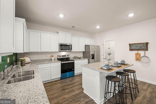 kitchen with stainless steel appliances, light stone counters, a sink, and white cabinets