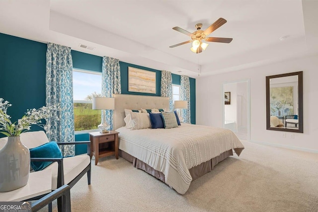 bedroom with a raised ceiling, visible vents, carpet flooring, and multiple windows