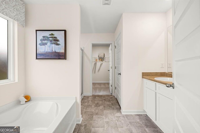 bathroom featuring baseboards, visible vents, a garden tub, a walk in closet, and vanity