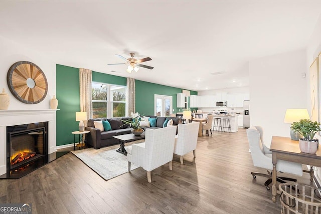 living room featuring a ceiling fan, a glass covered fireplace, and wood finished floors