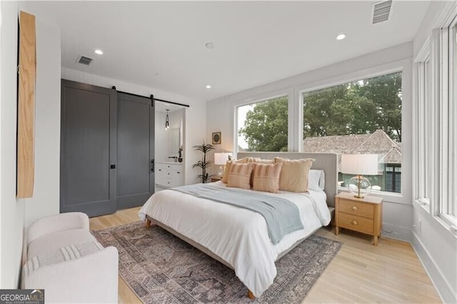 bedroom featuring light wood-type flooring, a barn door, visible vents, and baseboards