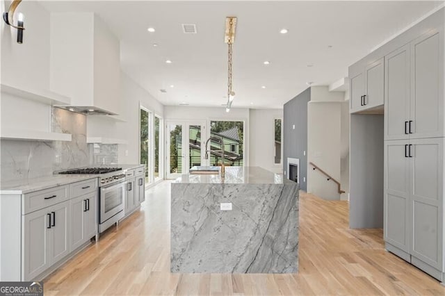 kitchen featuring stainless steel range, a spacious island, backsplash, light wood-style flooring, and light stone countertops