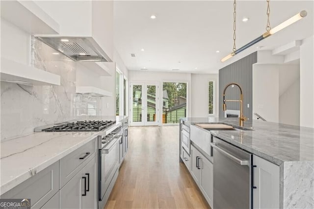 kitchen with appliances with stainless steel finishes, an island with sink, light stone counters, and white cabinetry