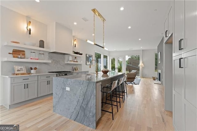 kitchen featuring a large island, custom range hood, light stone counters, a breakfast bar, and open shelves