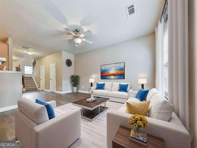 living area featuring ceiling fan, visible vents, baseboards, stairway, and light wood-type flooring