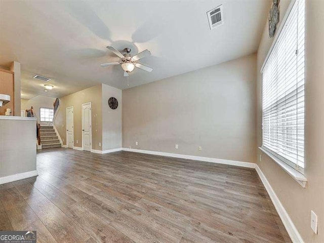 empty room with dark wood-style floors, visible vents, ceiling fan, baseboards, and stairs