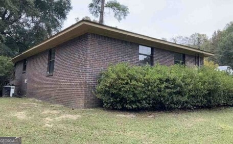 view of side of property featuring a yard, cooling unit, and brick siding