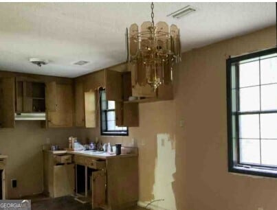 kitchen featuring brown cabinetry, a sink, visible vents, and a notable chandelier