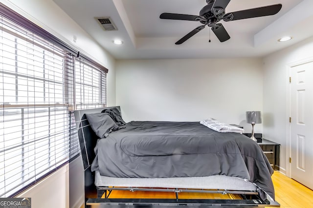 bedroom with light wood finished floors, a tray ceiling, visible vents, and recessed lighting