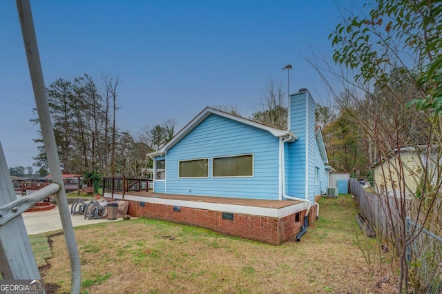 rear view of house with cooling unit, a yard, a chimney, and fence