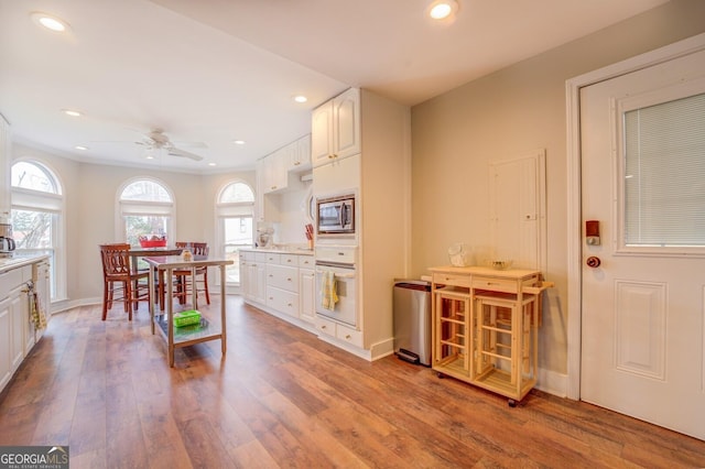 kitchen with white cabinets, light wood-style flooring, stainless steel microwave, white oven, and light countertops