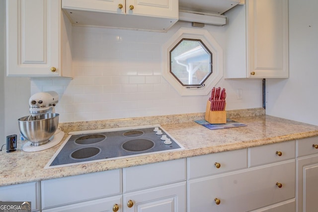 kitchen featuring decorative backsplash, white cabinets, light countertops, and electric stovetop