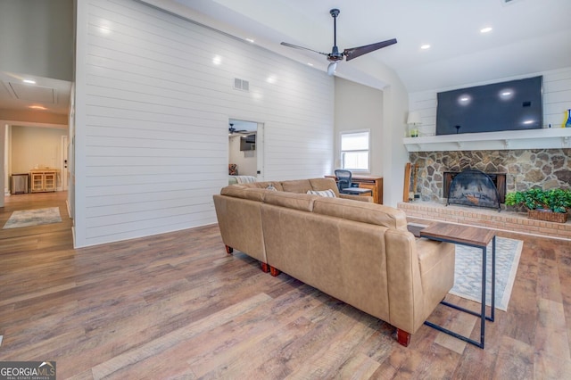 living area featuring attic access, visible vents, ceiling fan, wood finished floors, and a fireplace