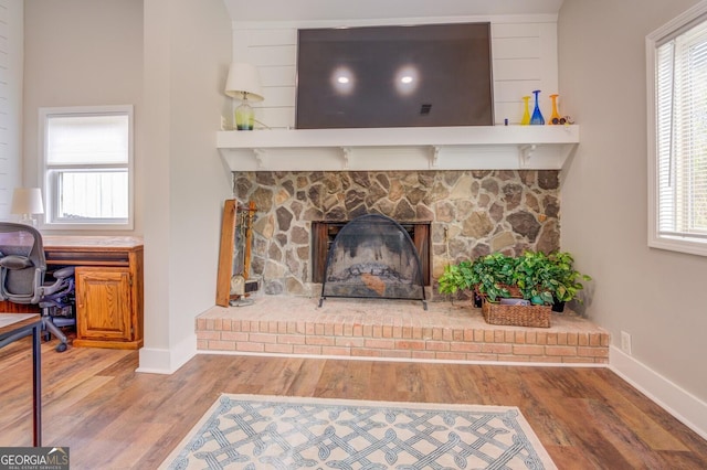 room details with a fireplace with raised hearth, baseboards, and wood finished floors