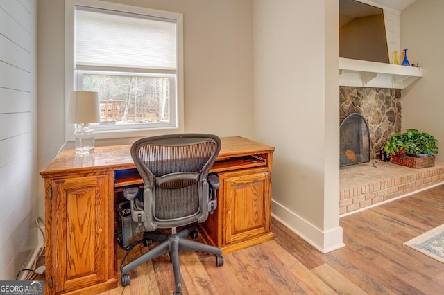 office area featuring light wood-type flooring, baseboards, and a stone fireplace