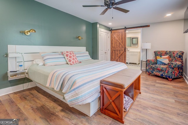 bedroom with a barn door, baseboards, wood finished floors, and recessed lighting