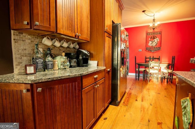 kitchen featuring decorative backsplash, freestanding refrigerator, hanging light fixtures, crown molding, and stone counters