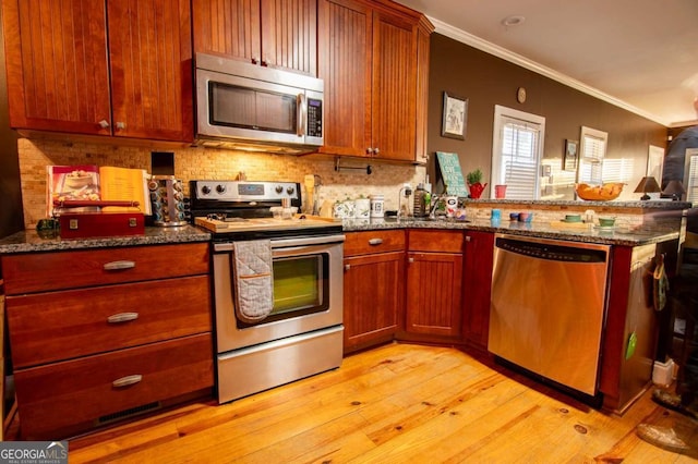 kitchen featuring light wood finished floors, ornamental molding, dark stone countertops, a peninsula, and stainless steel appliances