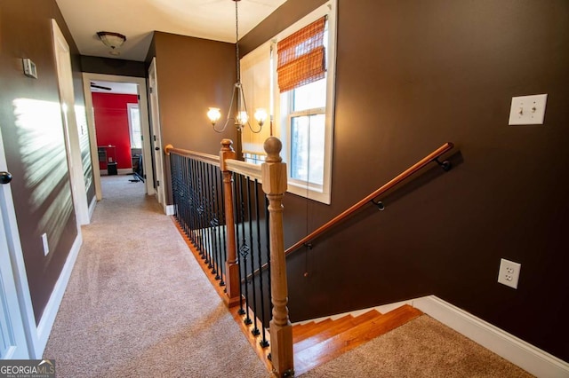 hall with carpet floors, an inviting chandelier, baseboards, and an upstairs landing