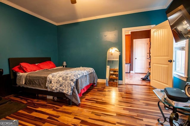 bedroom featuring crown molding, baseboards, arched walkways, and wood finished floors