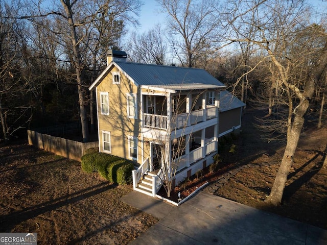 view of front facade with metal roof, a chimney, fence, and a balcony